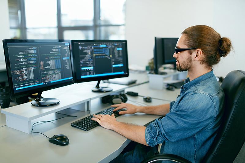 Programação. Homem trabalhando no computador no escritório de TI, sentado à mesa escrevendo códigos. Programador digitando código de dados, trabalhando em projeto na empresa de desenvolvimento de software. Imagem de alta qualidade.
